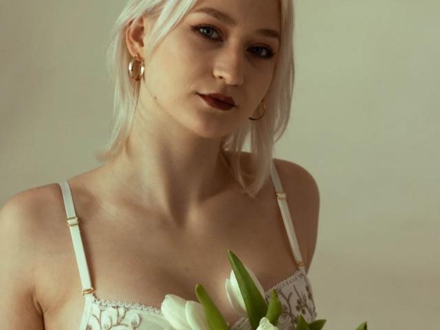 LilySweetBabe com pele clara, cabelo loiro platinado, brincos dourados, vestindo um sutiã de renda branco, segurando tulipas brancas, seios pequenos, sorriso discreto, iluminação suave, expressão delicada..