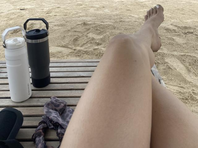 ValeryLombardi's legs are crossed on a wooden beach chair, with a white and black water bottle on the left and a tie-dye cloth on the right.