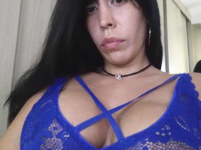SeleneBrigth, con i capelli neri, un anello al naso e orecchini a cerchio, indossa un reggiseno di pizzo blu con spalline incrociate, che mette in mostra il seno. Ha una collana nera con un piccolo cuore..