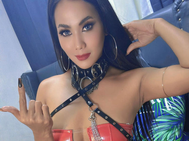 AddictiveMiss4u-hot with dark hair, hoop earrings, red lipstick, black leather harness, and a silver chain, showing off her tits and giving a peace sign.