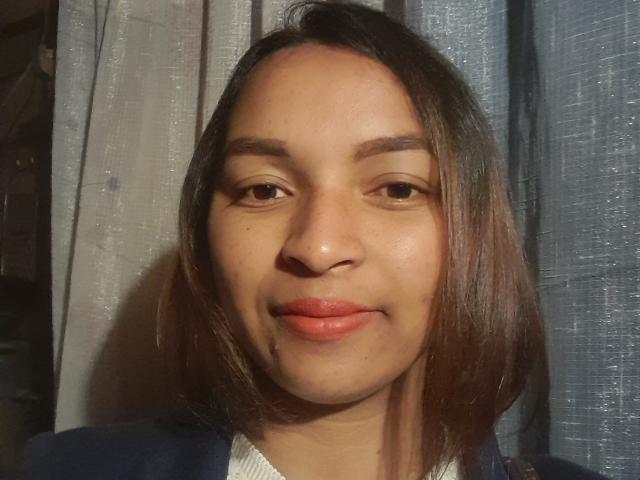Pouchitah has brown, straight shoulder-length hair, brown eyes, and a slight smile with pinkish-red lips. She's wearing a dark blue top with a white shirt underneath.
