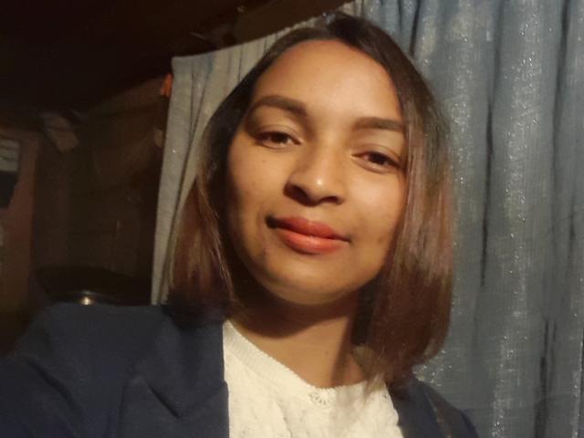 Pouchitah has medium brown skin, straight brown shoulder-length hair, and a subtle smile. She's wearing a blue blazer over a white top. Her lips are slightly parted.