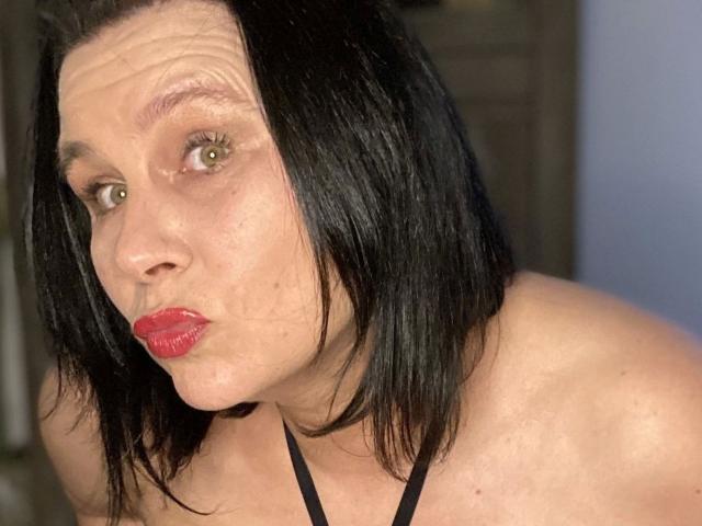 NsTempel-hot with black shoulder-length hair, red lipstick, and green eyes, pouting with a slight squint, wearing a black halter top, showing her bare shoulders.