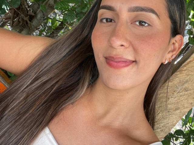 EmelyOwen has long brown hair, brown eyes, and a small nose piercing. She's smiling with pink lips, wearing a white top, and has a cute ear piercing.