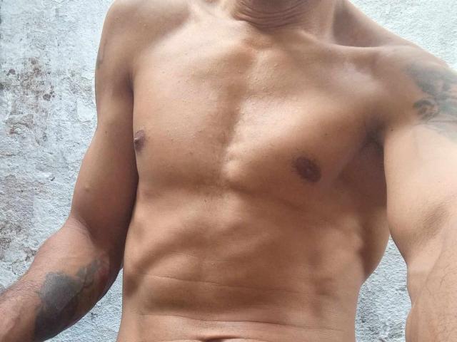 Robinsonn's toned, tan-skinned torso shows defined abs and small, dark nipples. His arms have tattoos, and a visible neck. His upper body is slightly muscular.