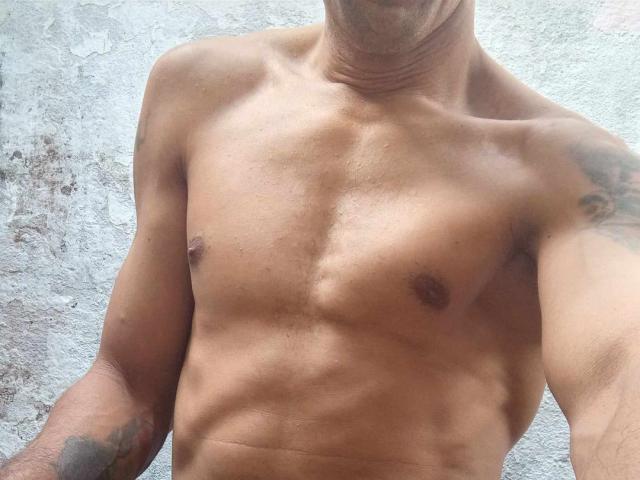 Robinsonn's toned, muscular chest with small, dark nipples and visible abs. He's shirtless, showing tattoos on his right arm, with a slightly tanned, smooth skin.