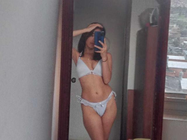 VennusGhirls with small tits, flat ass, and a cute pussy, wearing a light blue bikini, taking a mirror selfie, hand covering her head, holding a blue phone.