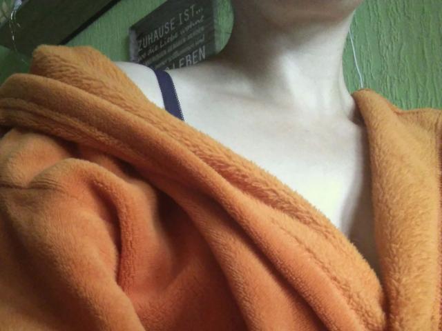 Jennylove-hot's pale skin, small tits, covered by an orange, fuzzy towel, with a dark blue strap visible on her shoulder.