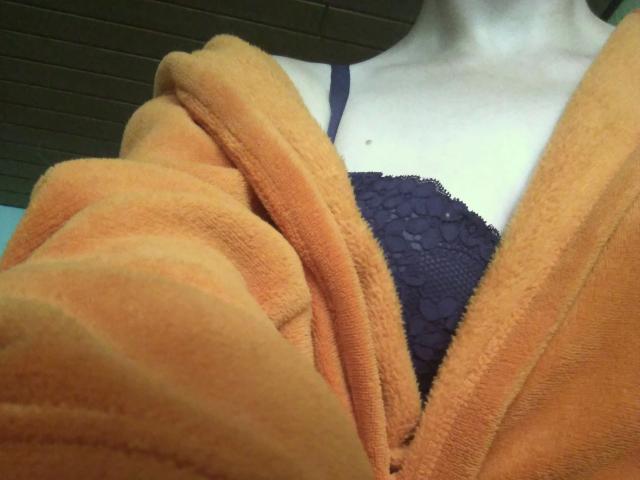 Jennylove-hot's orange towel is draped over her tits, revealing a black lace bra with a textured pattern. Her fair skin is partially visible.
