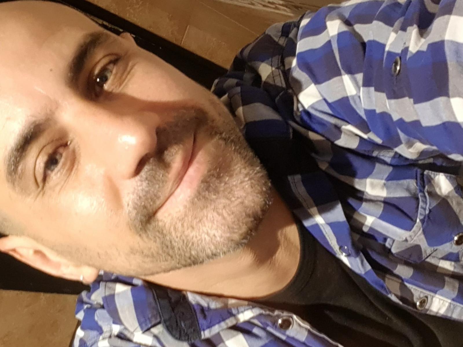 MartesHotHot heeft een kaal hoofd, lichtbruine huid, kleine bruine ogen en een getrimde baard. Hij draagt een blauw-wit geruit shirt en glimlacht lichtjes..