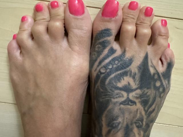 AndraD's feet with pink nail polish, showing a detailed black tattoo of a lion's face on the right sole. The tattoo covers her entire right foot.