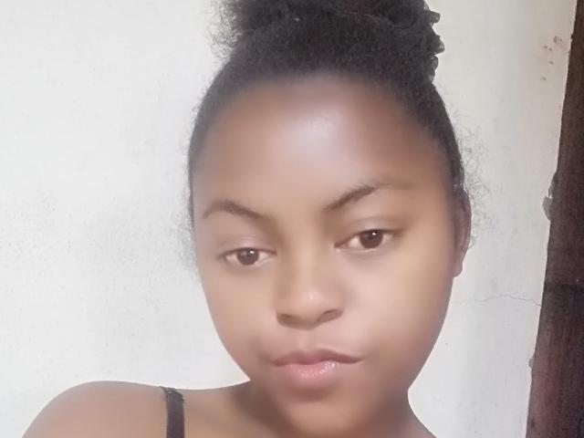 YlahXoxo has a dark brown skin tone, small nose, and slightly parted lips with a subtle pout. She has curly black hair in a bun and brown eyes.