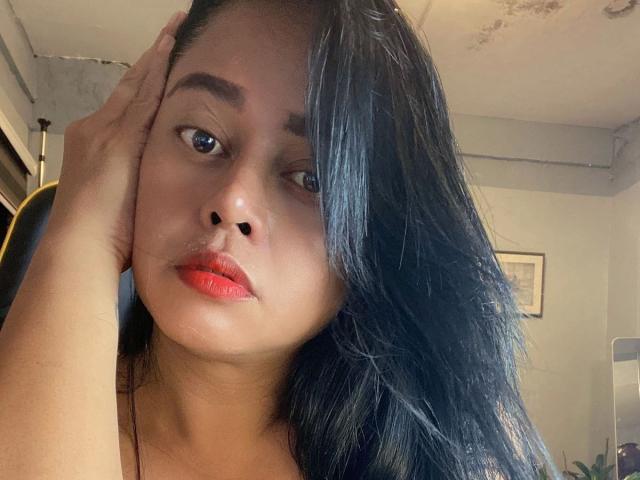 YENDYSFOX01-hot with black hair, red lipstick, and hand on head, looking serious. She has medium brown skin, blue eyes, and is wearing a black top.