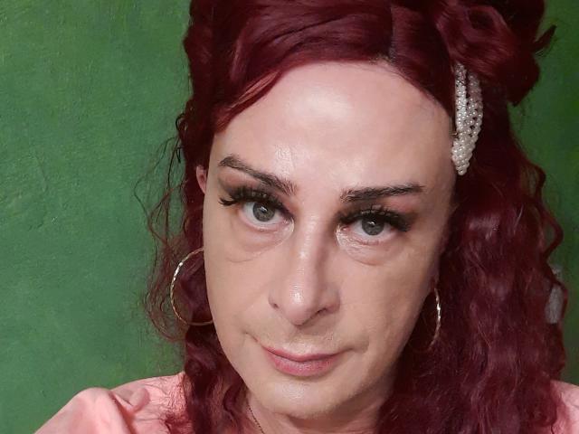 MandyLine has red curly hair, a pearl hair clip, hoop earrings, and long eyelashes. Her skin is shiny, and she's smiling slightly with her nose slightly upturned.