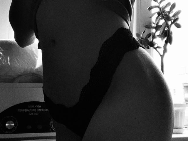 A parte inferior da barriga de JacquelynCelie e a calcinha de renda preta estão em destaque. Sua barriga plana e nádegas levemente curvadas são visíveis. A imagem é uma fotografia em preto e branco..