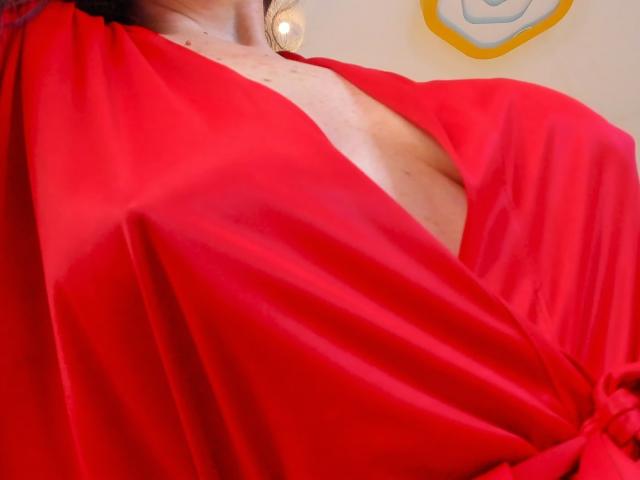 MimmyLongNipples in a red satin robe with a deep V-neck, exposing a bit of her bare chest and showing her tits. Robe is draped over her shoulders.