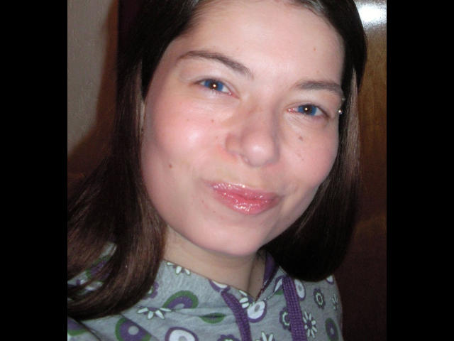Chiara177-hot has puffy pink lips, light skin, brown eyes with a small nose ring, and brown hair, wearing a grey patterned shirt, smiling slightly.
