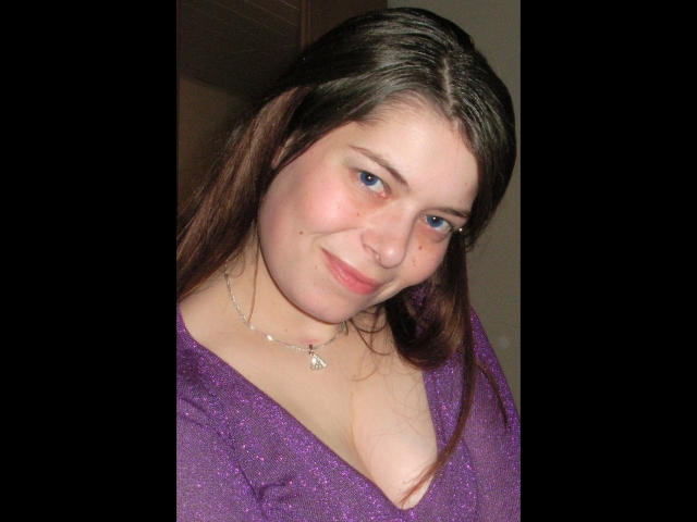 Chiara177-hot has blue eyes, brown hair, and a slight smile. She's wearing a purple sparkly top with a low neckline, showing her tits. She's also wearing a necklace.