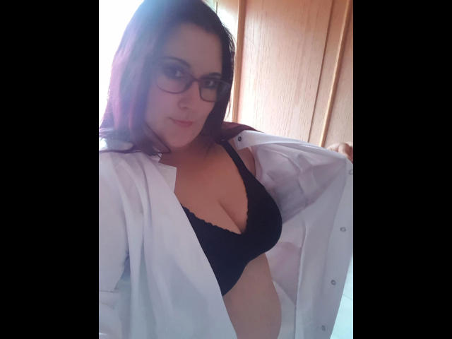 JosySweet-hot with glasses, light skin, red-brown hair, black lace bra, and open white shirt, showing her tits and a slight smile. Wooden door in background.
