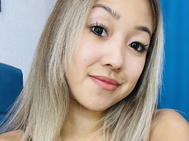 RenyLime a la peau brun clair, les cheveux blonds et les cils noirs. Elle sourit, avec des lèvres roses, une petite imperfection sur la joue et un visage mignon. Ses seins ne sont pas visibles..