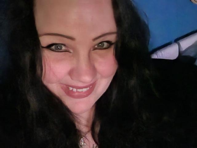 Blackbeauty43-hot with long black curly hair, green eyes, and a cute smile, showing her pinkish lips and slightly flushed face in a selfie. Her tits are not visible.