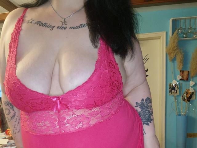 Blackbeauty43-hot with large tits in a pink lace lingerie top, showing tattoos on arms, wearing a necklace, and black hair. Her chest is prominent with a small pink bow.