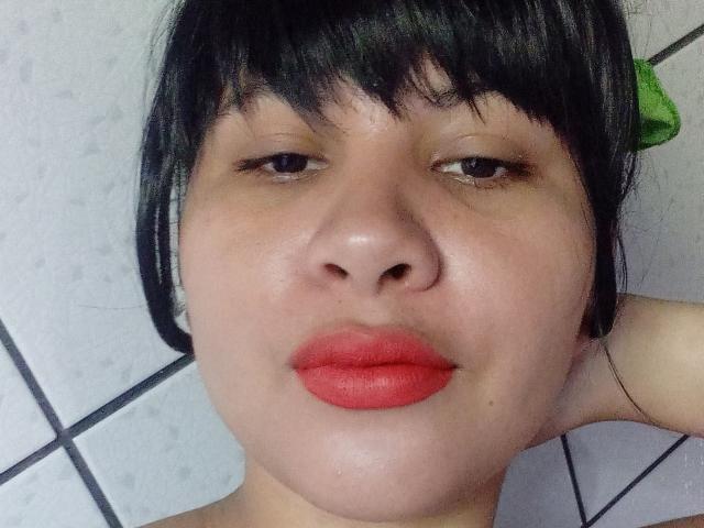 YaraOk has a chubby face with red lipstick, black bangs, and a green hair clip on the right side, looking straight at the camera with slightly droopy eyes.