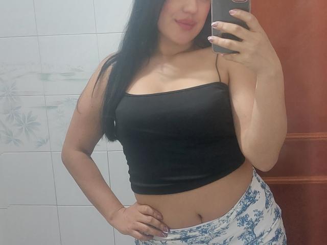 LauraRichis with long black hair, wearing a black strapless top, showing her tits and a hint of her pussy, holding a phone, and smiling in a mirror selfie.