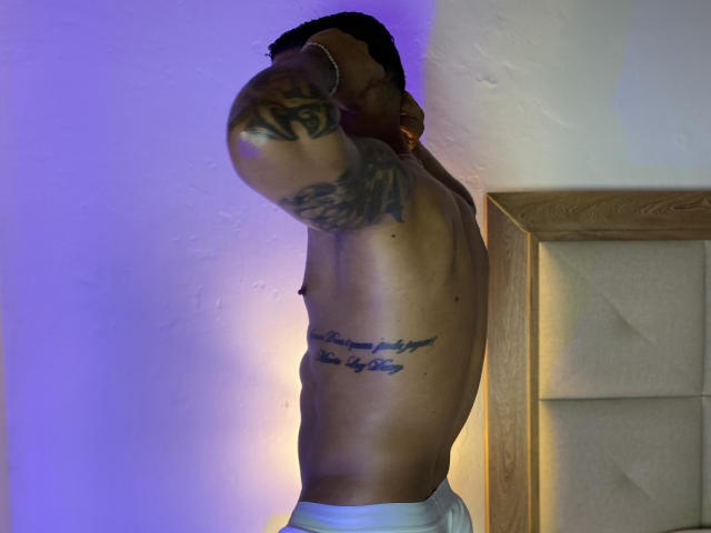 EvaAndMarcelo, shirtless, muscular, tattooed arm, raised arm, blue and yellow light, white underwear, wooden headboard, side profile, toned abs, dark hair, gold earrings, slight tan.