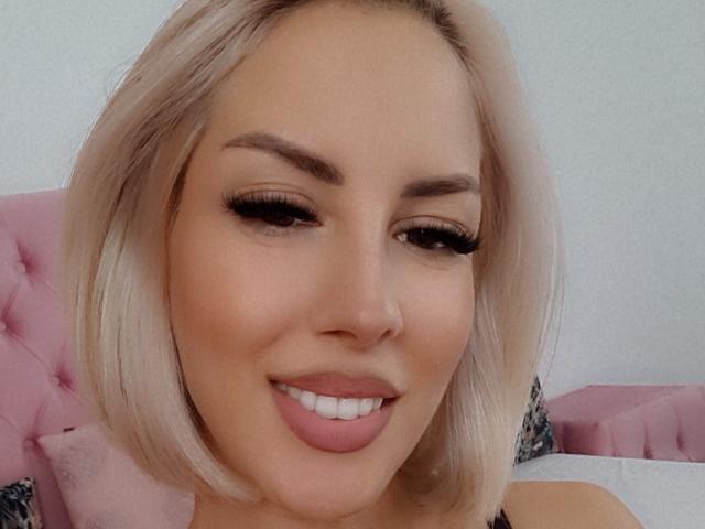 LanieHotXX has blonde bob, thick eyebrows, long lashes, and is smiling with pink lipstick. Her nose is pierced. She's looking slightly to the side, showing off her cute ass.