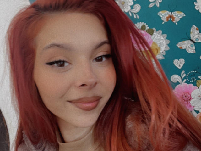 Bellefrancaise69 has red hair, light skin, black eyeliner, and a subtle smile. Her pink lips and slight nose are visible. She's looking to the side, showing her face.