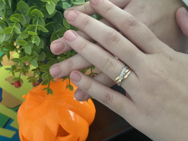 Steisii's hands with pink nails, a gold ring with a diamond, and a small orange pumpkin in the background. Green leafy plant to the left.