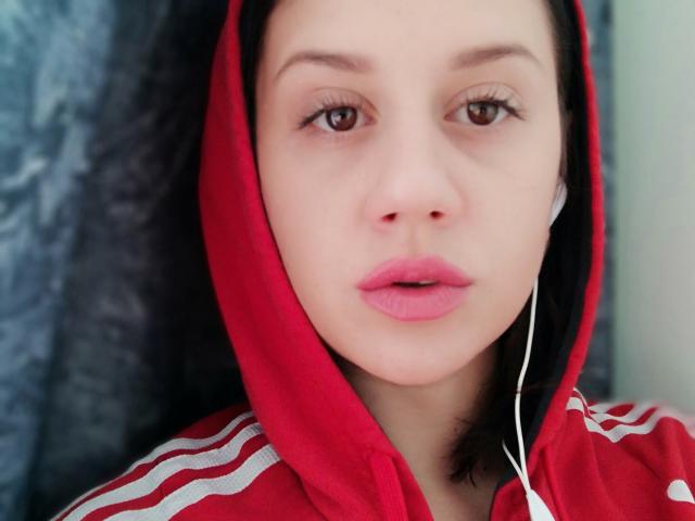 SamanthaApple with fair skin, brown eyes, and pink lips, wearing a red hoodie with white stripes, earbuds in, looking forward, black hair peeking out.