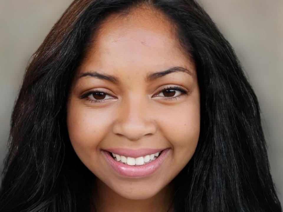 PegySexy has dark brown eyes, long black hair, and a smile showing white teeth. Her skin is a warm brown tone, and she's wearing pink lipstick.