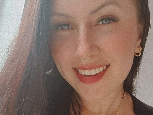 LuisaV has a cute smile with red lipstick, blue eyes, long brown hair, gold nose ring, crescent moon earring, and gold necklace. Her tits aren't visible.