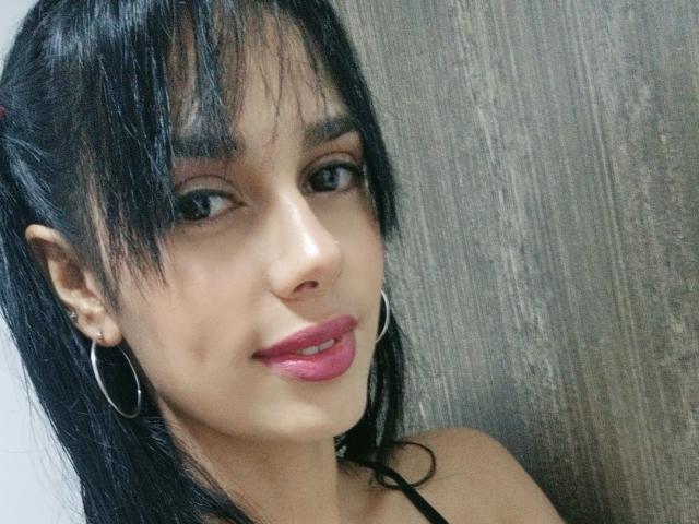 AnaisHilton with black hair, pink lipstick, hoop earrings, and a slight smile, showing her smooth, tan skin and pretty face. Her tits are not visible.