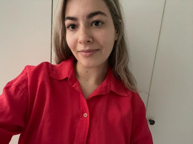 FancyRosie with blonde hair, wearing a red shirt, smiling slightly, brown eyes, light skin, small nose, and a tiny mole on her chin. Boobless, no visible ass or pussy.