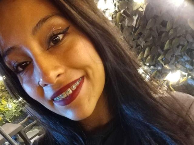 NoremCute has a cute smile with red lipstick, straight black hair, and a nose ring. She's showing off a set of shiny, metallic braces on her teeth.