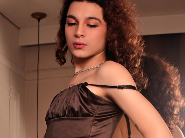 CrystalCraze with curly brown hair, wearing a brown satin dress, has a chain necklace, and has her eyes half-closed with pink lipstick on her soft-looking face.