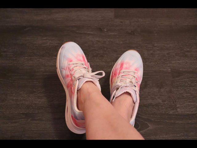 HerrinDeluxe-hot's legs in white and pink sneakers with slightly dirty soles, standing on dark wooden floor. Her toes are slightly pointed, showing the laces are untied.