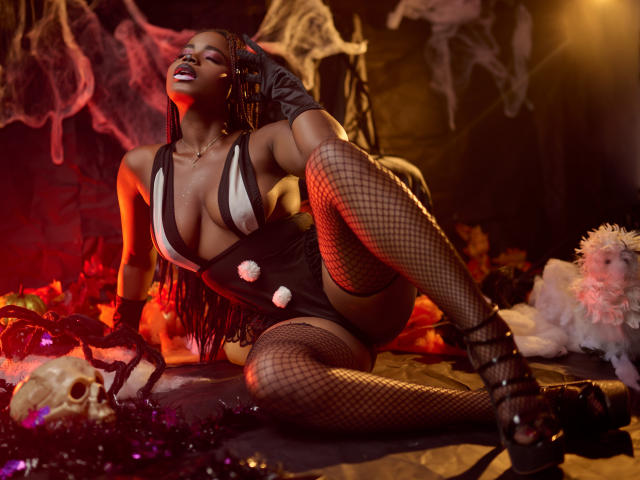 LindaBird with dark skin, big boobs, and a curvy ass, wearing a black and white outfit, fishnet stockings, and high heels, posing seductively with a skull and smoke.