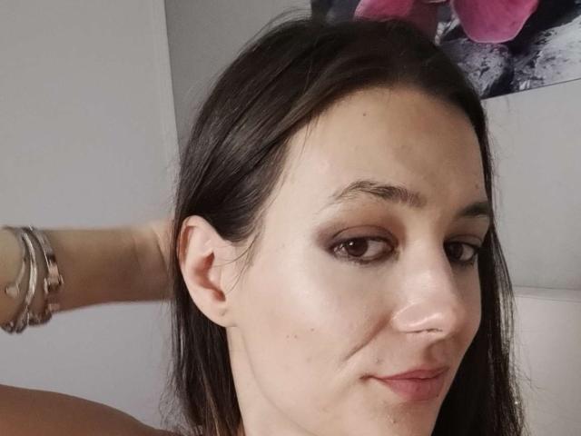 JuliaHuntis has pale skin, brown eyes, and dark brown hair. She's smiling slightly with her hand behind her head, wearing silver bracelets. Her nose is pierced.