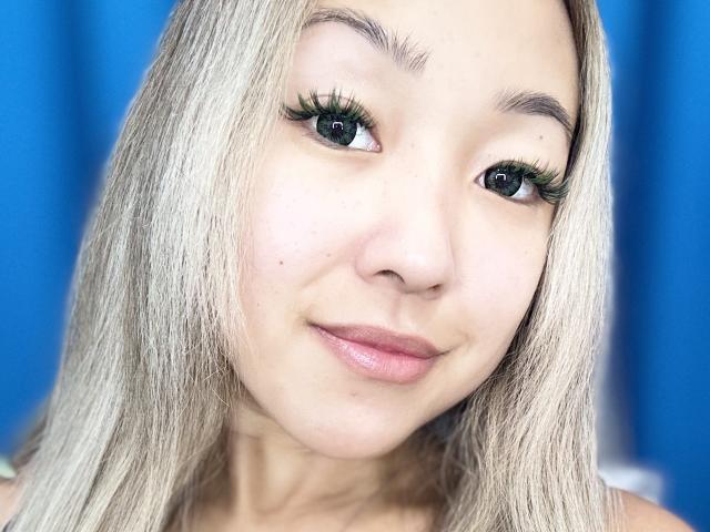 RenyLime has long, blonde hair, green eyeliner, and a slight smile. Her eyes are dark and she has a small beauty mark near her right nostril.