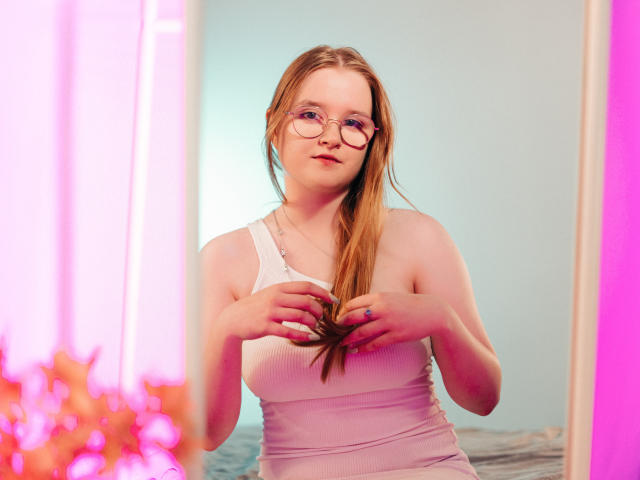 BonnieBell with glasses, pale skin, and red hair, wearing a white tank top, standing, hands in her hair, pink and purple lighting, soft focus, mirror reflection.