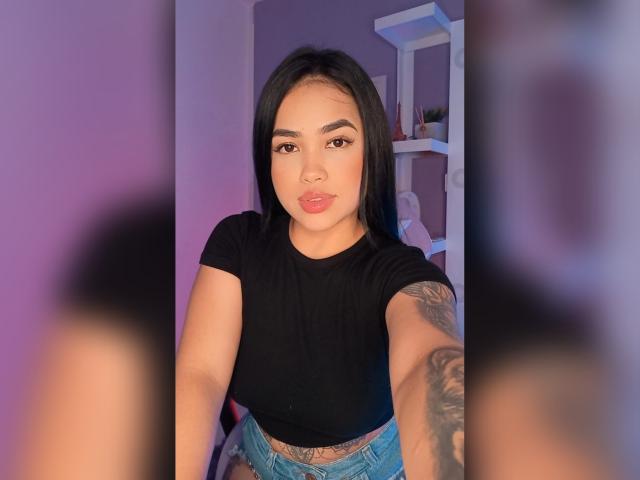 Celeste Villamizar, avec ses cheveux noirs, portant un haut noir et un jean bleu, montrant un tatouage sur son bras droit, prenant un selfie, avec des lèvres roses et une expression mignonne..