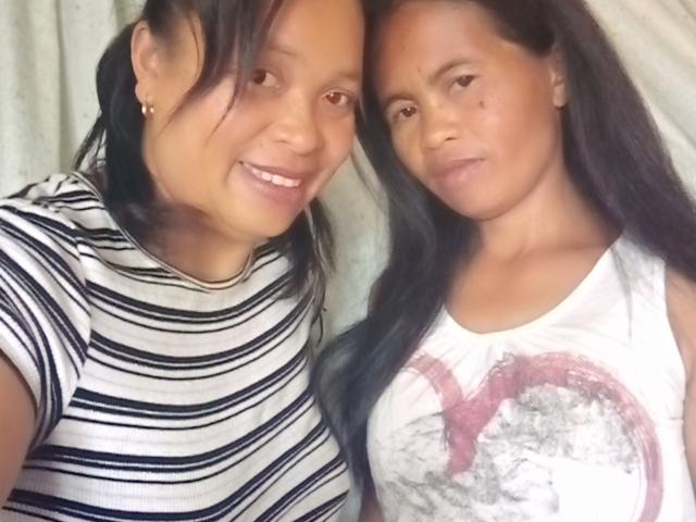 Two sexy Black women, smiling and standing close. One has striped shirt, long black hair, small earrings. Other wears white tee with red graphic, long black hair.