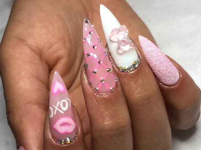 Les ongles de SheylaSpooner sont étranges, avec des motifs roses, blancs et roses pailletés, ainsi que des autocollants en forme de cœur et de lèvres, des strass, et des ongles roses et blancs texturés..
