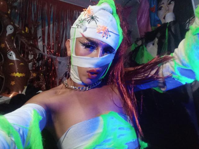 Crystallnn with glowing green and blue lights, wearing a white mask, bandage around face, white strapless top, choker, and red braids, pulling hair, in dark room.