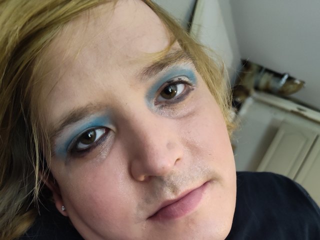 Ava Brayns ha l'ombretto azzurro, i capelli biondi e un leggero baffo. Indossa una maglietta nera e ha degli orecchini piccoli. I suoi occhi marroni sono rivolti verso la fotocamera..