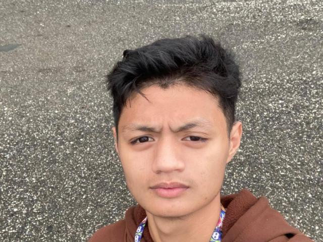 LucasSoHot has a neutral, slightly annoyed expression, short black hair, and is wearing a brown hoodie with a colorful necklace. His face is slightly sweaty.